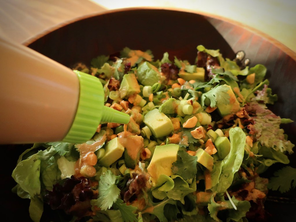 Squeeze bottle putting sesame-ginger dressing on a green salad