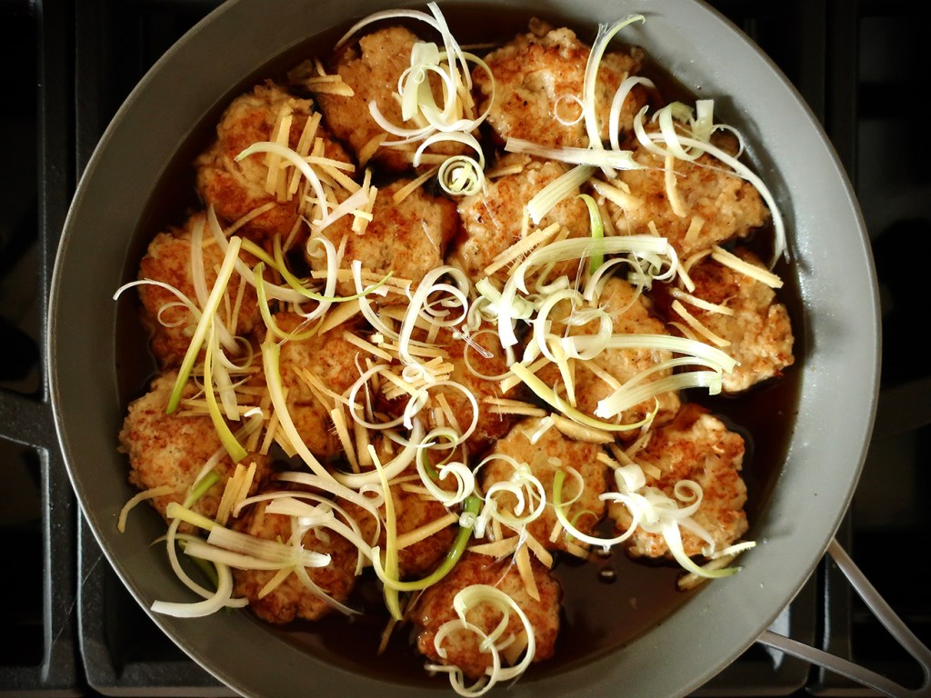 Chicken mini-burgers in Japanese yakitori-style sauce in a pan with with green onions and ginger