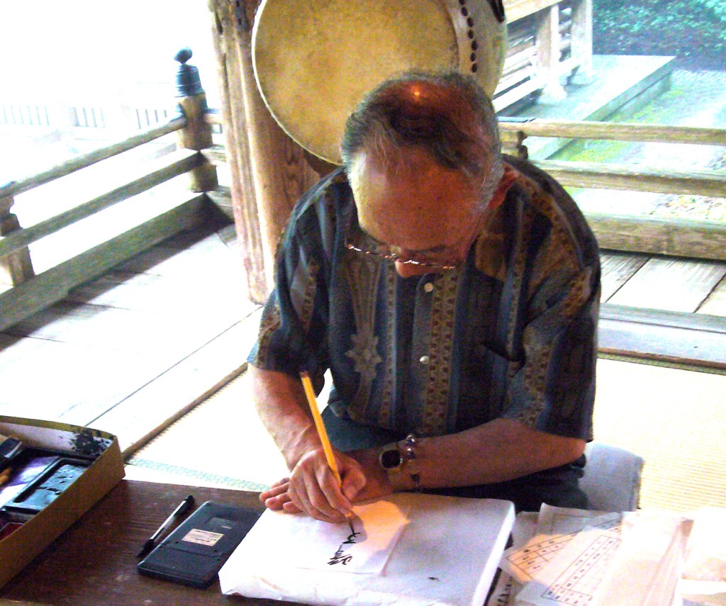 Man at a temple making a page for goshuin Japanese pilgrimage book