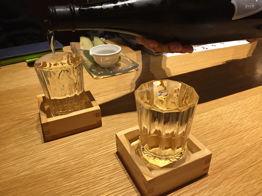 Pouring overflowing sake in cups standing in wooden boxes
