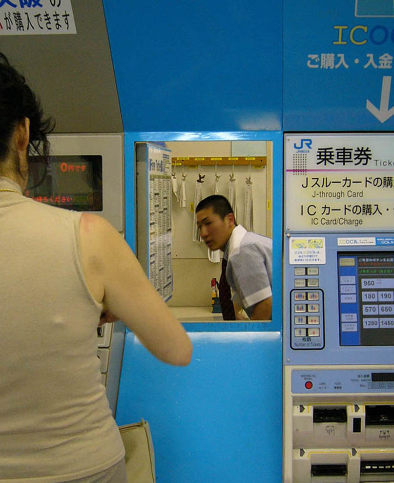 Station employee seen through the small door between Japanese train station ticket machines