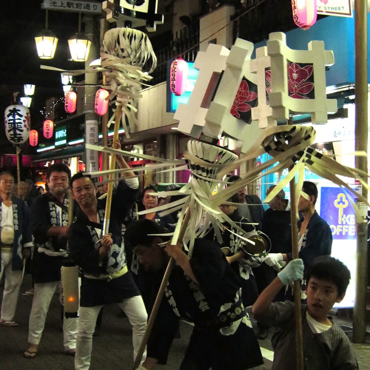 Photo of firemen twirling standards at night at the oeshiki ikegami festival in Tokyo
