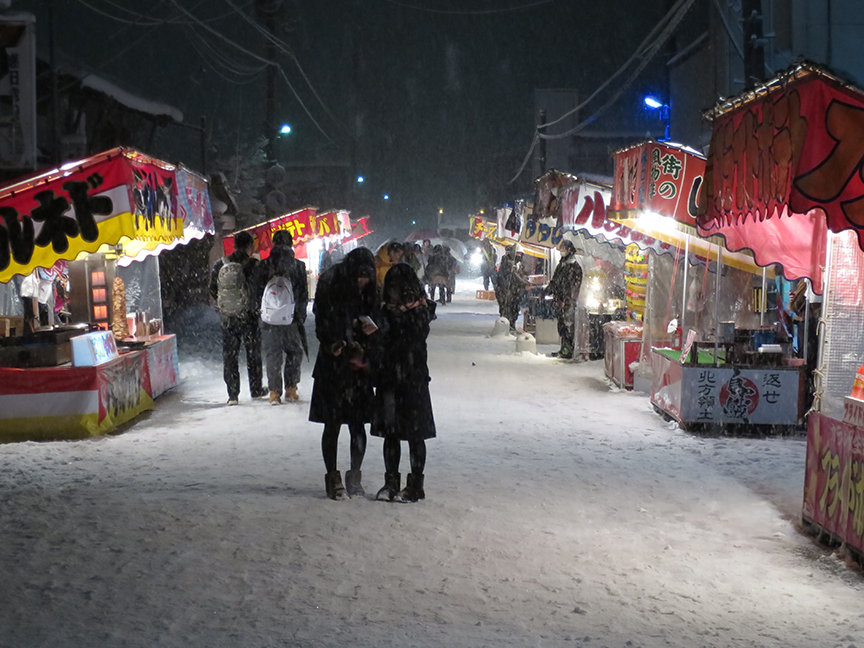 Food booths lining a street in the snow at the Kamakura Matsuri