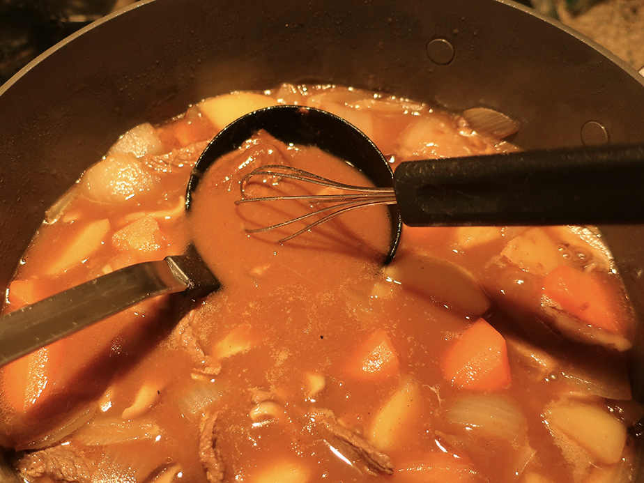 Stirring roux into curry rice using a ladle and whisk